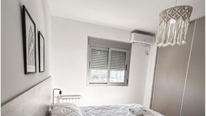 A bedroom with a large bed, a window with blinds, a radiator, and a hanging light fixture. - Cómodo dpto. en Salta para dos personas (Salta)