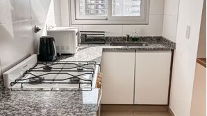 A modern kitchen with white cabinets, a gas stove, a microwave, and a window with a city view. - Cómodo dpto. en Salta para dos personas (Salta)
