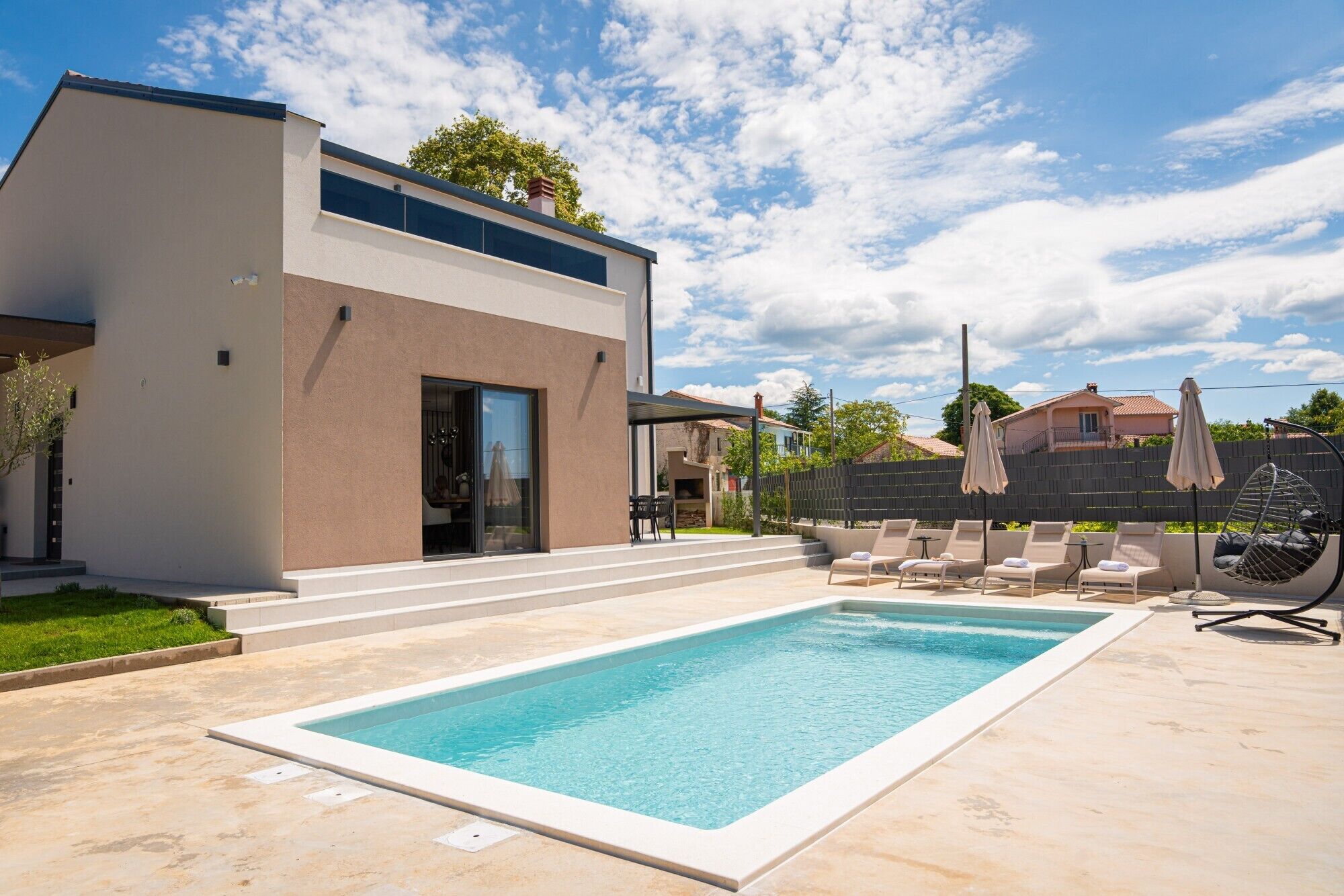 A modern house with a swimming pool, outdoor seating, and a covered patio.