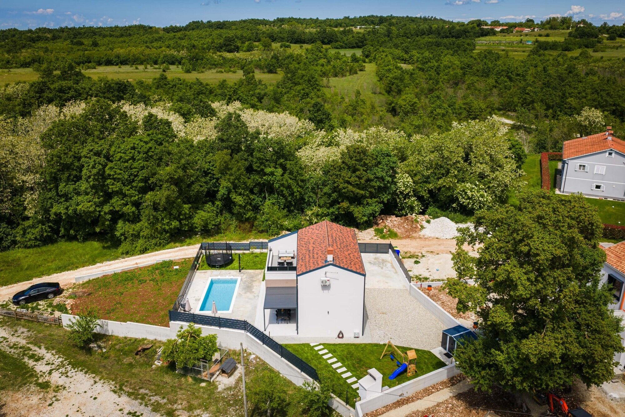 Ein Wohnhaus mit Schwimmbad, umzäunter Garten und Blick auf einen bewaldeten Bereich.