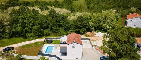 Ein Wohnhaus mit Schwimmbad, umzäunter Garten und Blick auf einen bewaldeten Bereich.
