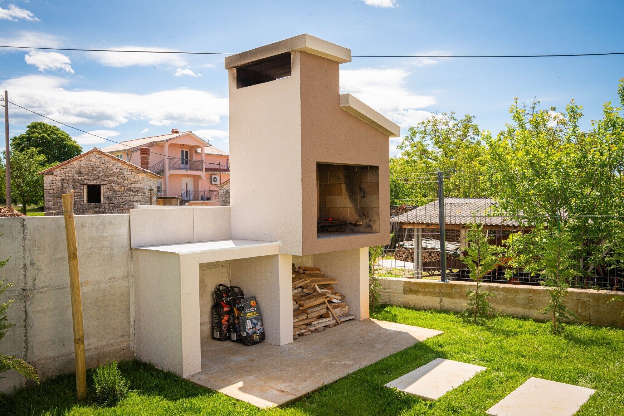 Una pequeña zona de cocina al aire libre con chimenea, una pila de leña y una bolsa de carbón.