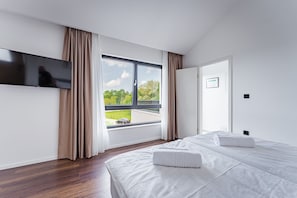 Ein modernes Hotelzimmer mit großem Fenster, einem Flachbildfernseher, einem Bett mit weißer Bettwäsche und einer Tür.