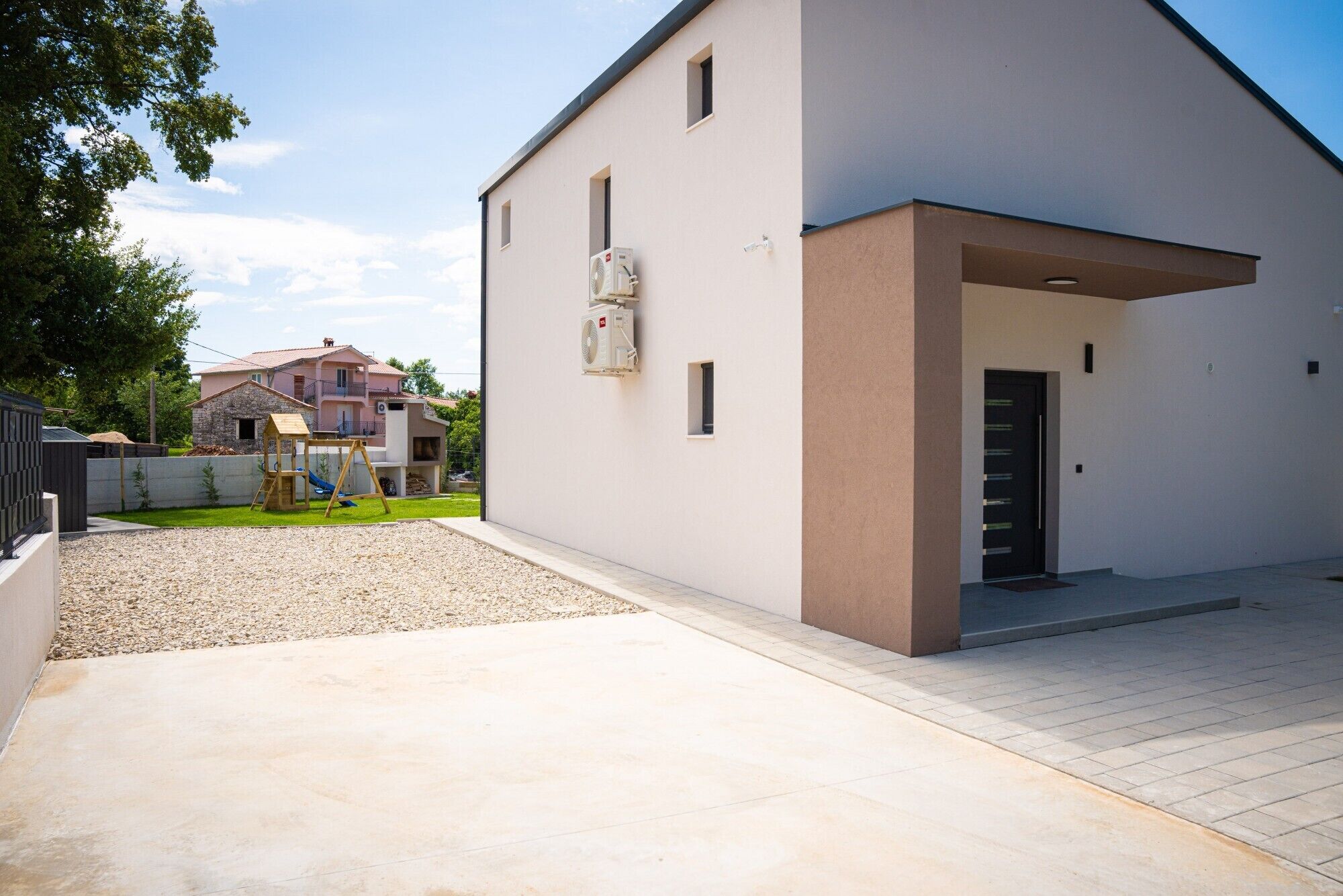 A modern two-story building with a flat roof, a covered entrance, and a gravel driveway.