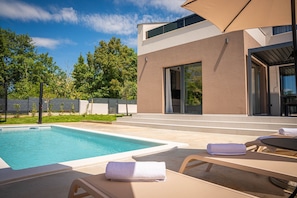 Ein modernes Haus mit Swimmingpool, Sitzgelegenheiten im Freien und einer überdachten Terrasse.