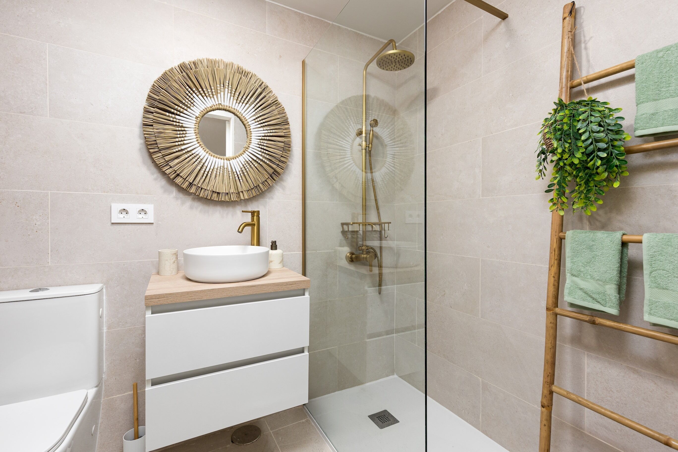 Un baño con ducha envuelta en vidrio, un espejo redondo, un lavabo blanco y un mueble de tocador de madera.