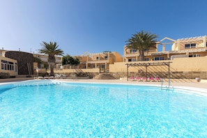 A swimming pool with clear blue water, surrounded by buildings with balconies and palm trees. - Home2Book Chill Terrace & Pool Escape Costa Calma (Costa Calma)
