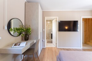 Ein modernes Schlafzimmer mit einem Bett, einem Schreibtisch mit Stuhl, einem Fernseher und einem durch eine offene Tür einsehbarer Badezimmer.