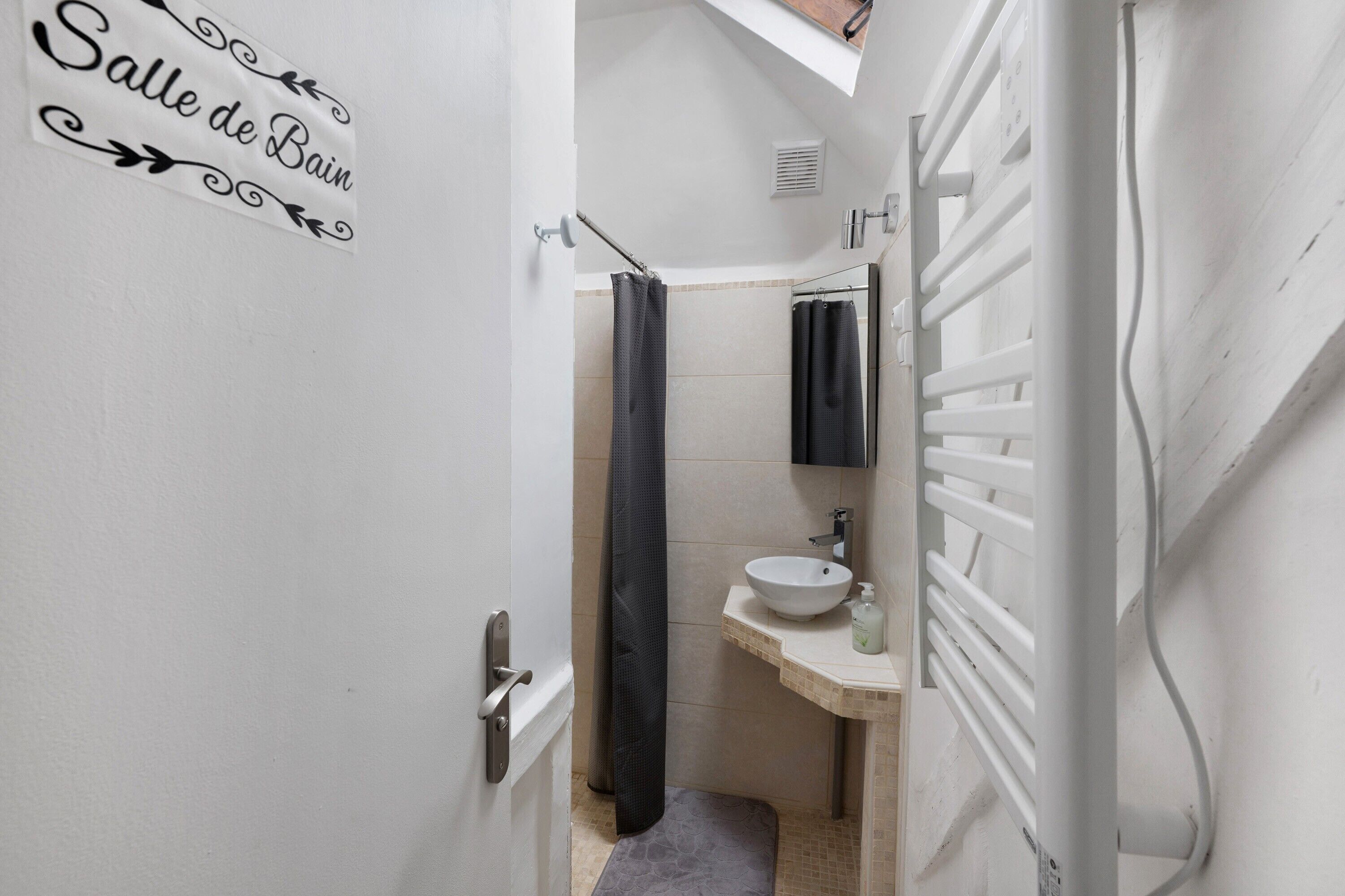 Une petite salle de bain avec une porte blanche, un porte-serviettes, un lavabo et un rideau de douche.