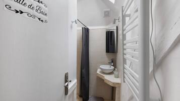 Een kleine badkamer met een witte deur, een handdoekhouder, een wastafel en een douchegordijn.