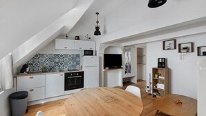 Een compacte keuken met witte kastjes, een houten eettafel en een klein bijzettafeltje.