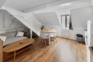 Una habitación estilo loft con piso de madera, un sofá, una mesa de comedor con sillas, una pequeña cocina y una escalera.