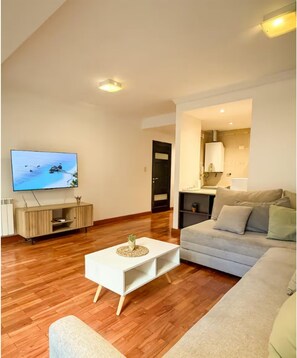 Uma sala de estar com televisão, sofá, mesa de centro e porta que dá para um banheiro.