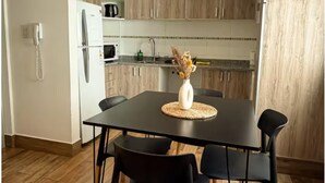 Eine moderne Küche mit Holzschränken, einem schwarzen Esstisch mit vier Stühlen und einer Vase mit Trockenblumen darauf.