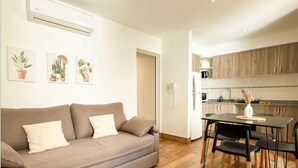 Ein modernes Wohnzimmer mit einer Couch, einer Essecke mit Tisch und Stühlen sowie einer Küche mit Holzschränken.