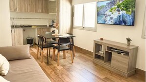 Ein modernes Wohnzimmer mit einer Couch, einem Essbereich mit Stühlen, einem an der Wand befestigten Fernseher und einer Küche im Hintergrund.