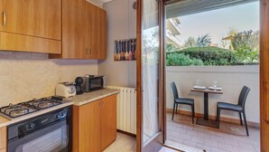 A kitchen with wooden cabinets, a gas stove, a microwave, and a toaster. There is a sliding glass door leading to a balcony with two chairs and a table. - Apartment 'Garda Lake' with Shared Pool, Private Terrace, and Air Conditioning (Desenzano del Garda)