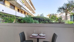 A table with two chairs and a glass on it, positioned against a wall with a view of a building and greenery. - Apartment 'Garda Lake' with Shared Pool, Private Terrace, and Air Conditioning (Desenzano del Garda)