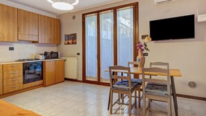 A kitchen with wooden cabinets, a stove, and a microwave. There is a dining area with a table and chairs. - Apartment 'Garda Lake' with Shared Pool, Private Terrace, and Air Conditioning (Desenzano del Garda)