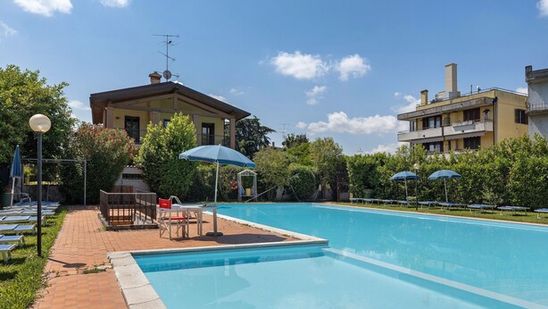 A swimming pool with lounge chairs and umbrellas, surrounded by buildings and greenery. - Apartment 'Garda Lake' with Shared Pool, Private Terrace, and Air Conditioning (Desenzano del Garda)