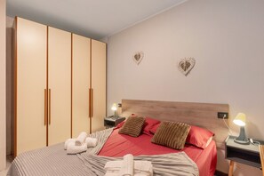 Een slaapkamer met een bed, twee nachtkastjes, een kledingkast en wanddecoraties in de vorm van harten.