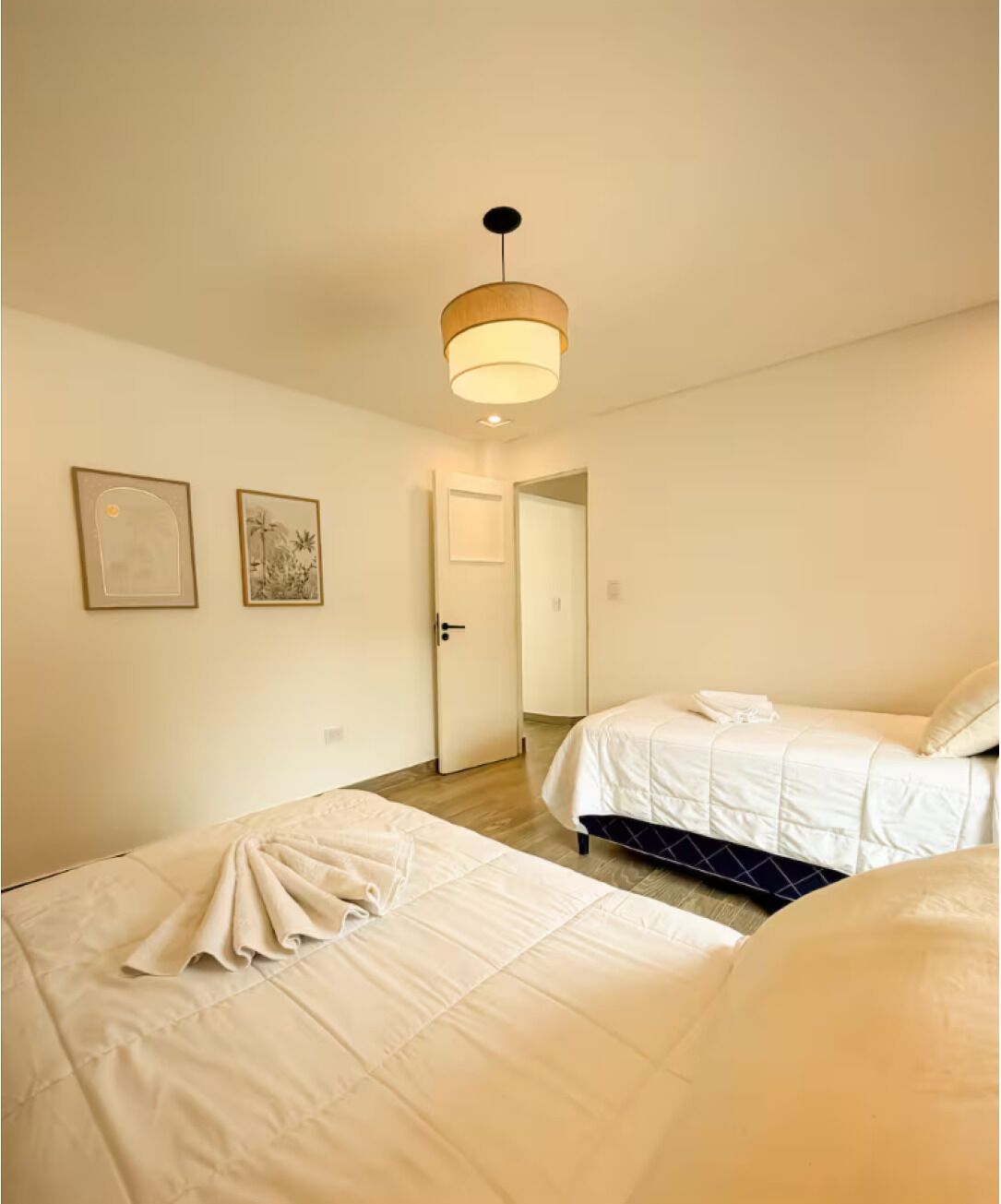 A hotel room with two beds, a door, and a ceiling light.