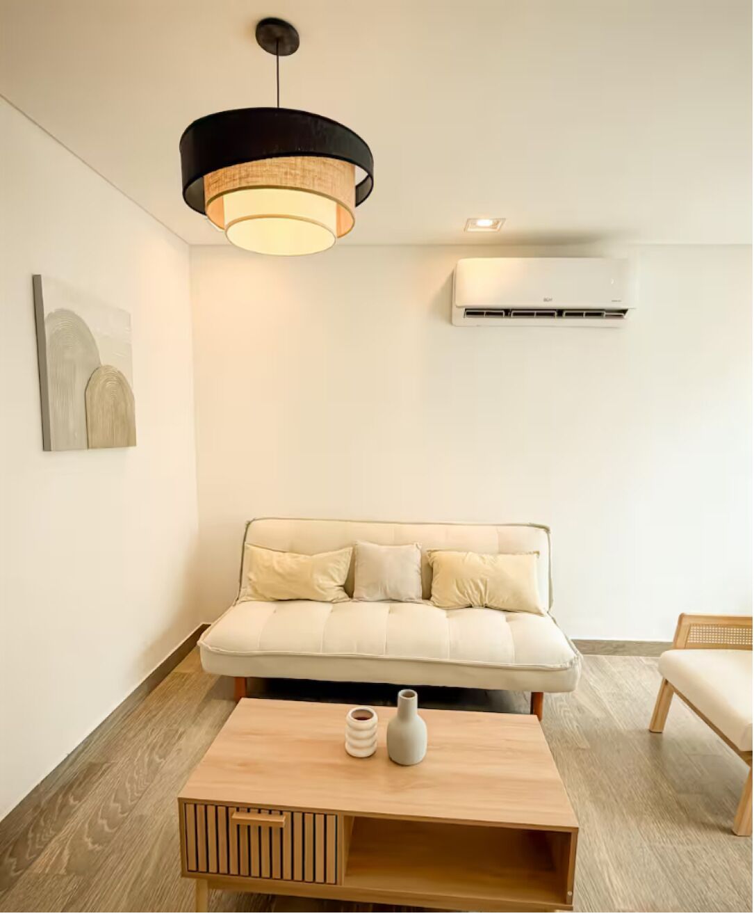 A modern living room with a sofa, a coffee table, a hanging light fixture, and an air conditioning unit.