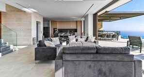 Ein modernes Wohnzimmer mit einer grauen Sofagarnitur, einem Essbereich und Blick auf den Ozean.