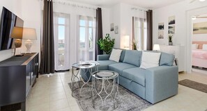 A modern living room with a sofa, two side tables, a TV, and a balcony with curtains. - Apartment PA11 - Callysta (Kouklia)