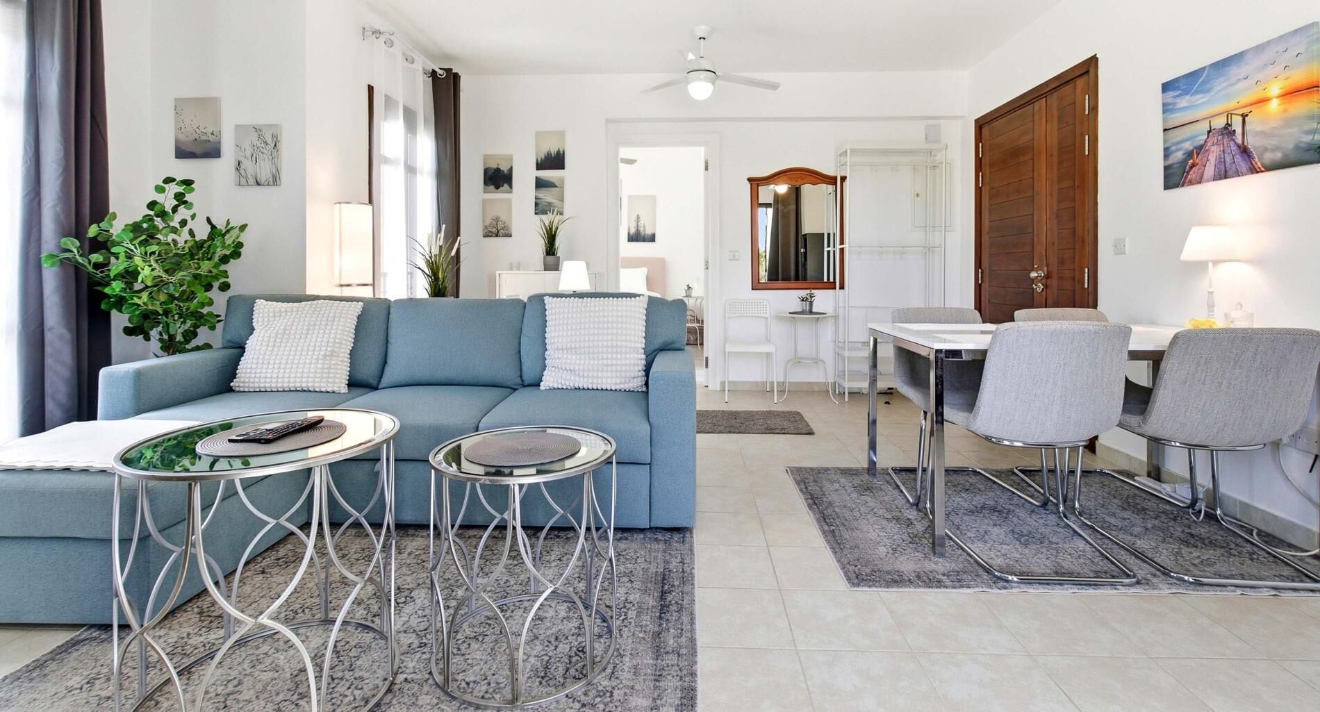 A living room with a sofa, two side tables, a dining area with a table and chairs, and a hallway leading to a bedroom.