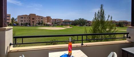 A balcony with a view of a golf course, a bottle, and a menu on a table.