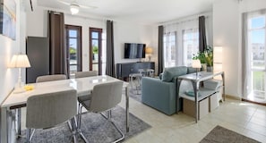 A modern hotel room with a dining area, a sofa, a TV, and a desk with a lamp. - Apartment PA11 - Callysta (Kouklia)