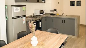 A modern kitchen with grey cabinets, a white refrigerator, a microwave, and a wooden dining table with a vase. - Dpto. a media cuadra de la plaza principal 2 (Salta)