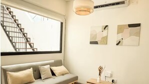 A modern living room with a sofa, a small wooden side table, a hanging light fixture, and abstract wall art. - Dpto. a media cuadra de la plaza principal 2 (Salta)