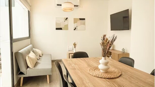 A modern dining area with a wooden table, chairs, a sofa, and pendant lighting. - Dpto. a media cuadra de la plaza principal 2 (Salta)