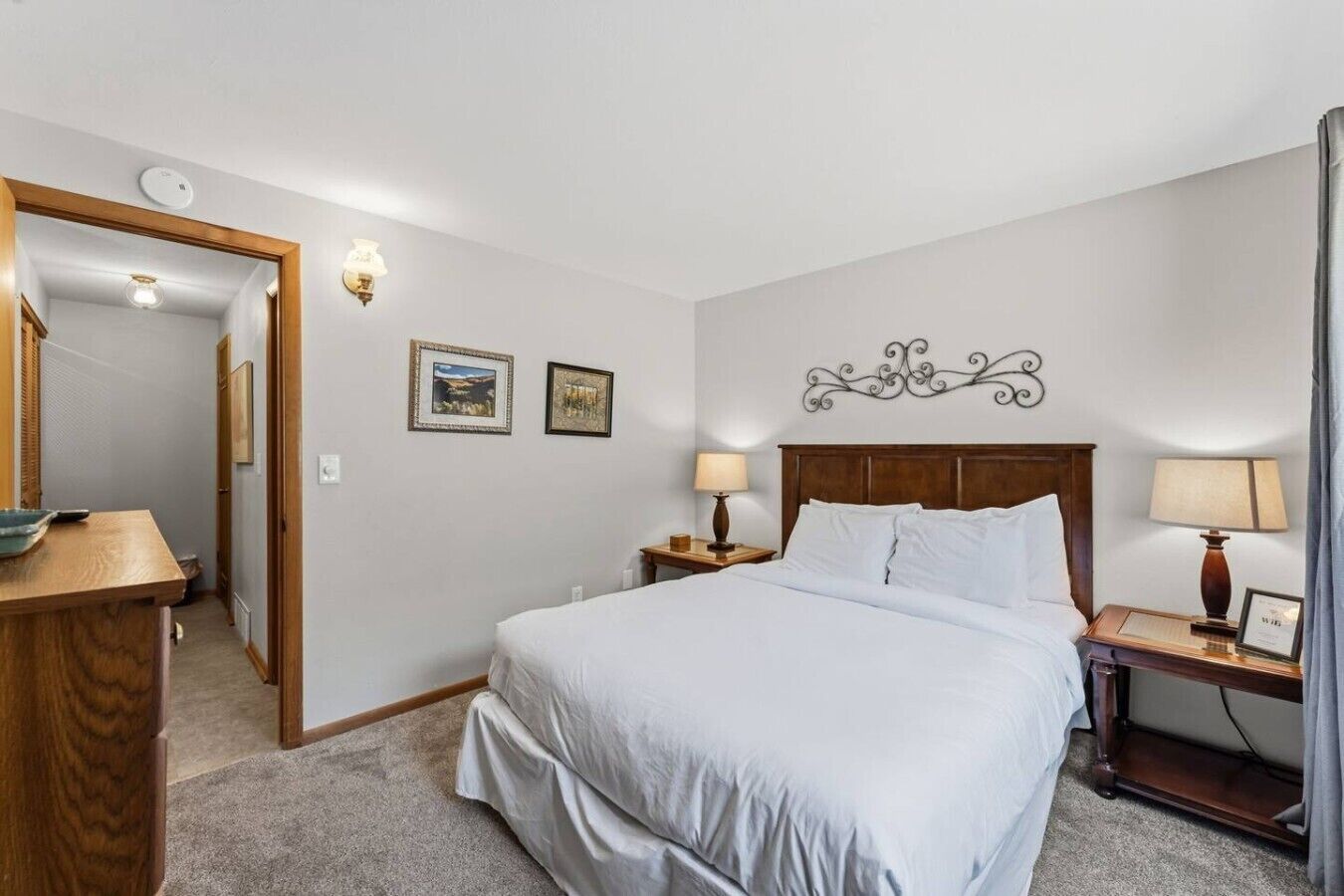 Habitación de hotel con cama, dos mesitas de noche con lámparas, un espejo y un adorno en la pared.