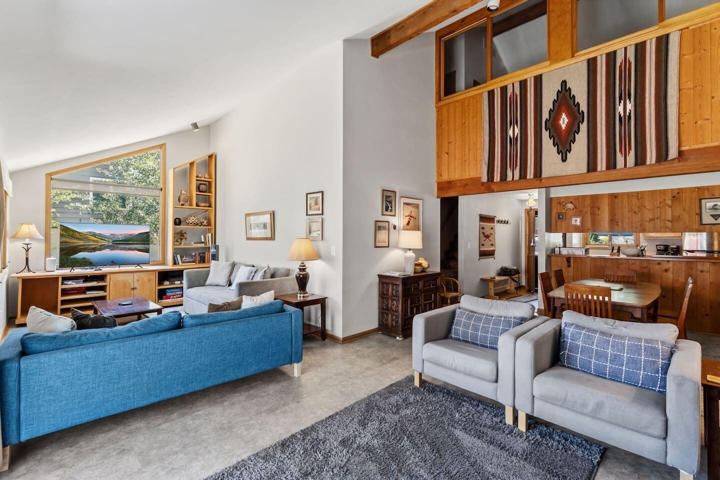 Una sala de estar moderna con un sofá azul, un sofá gris y un comedor con mobiliario de madera.