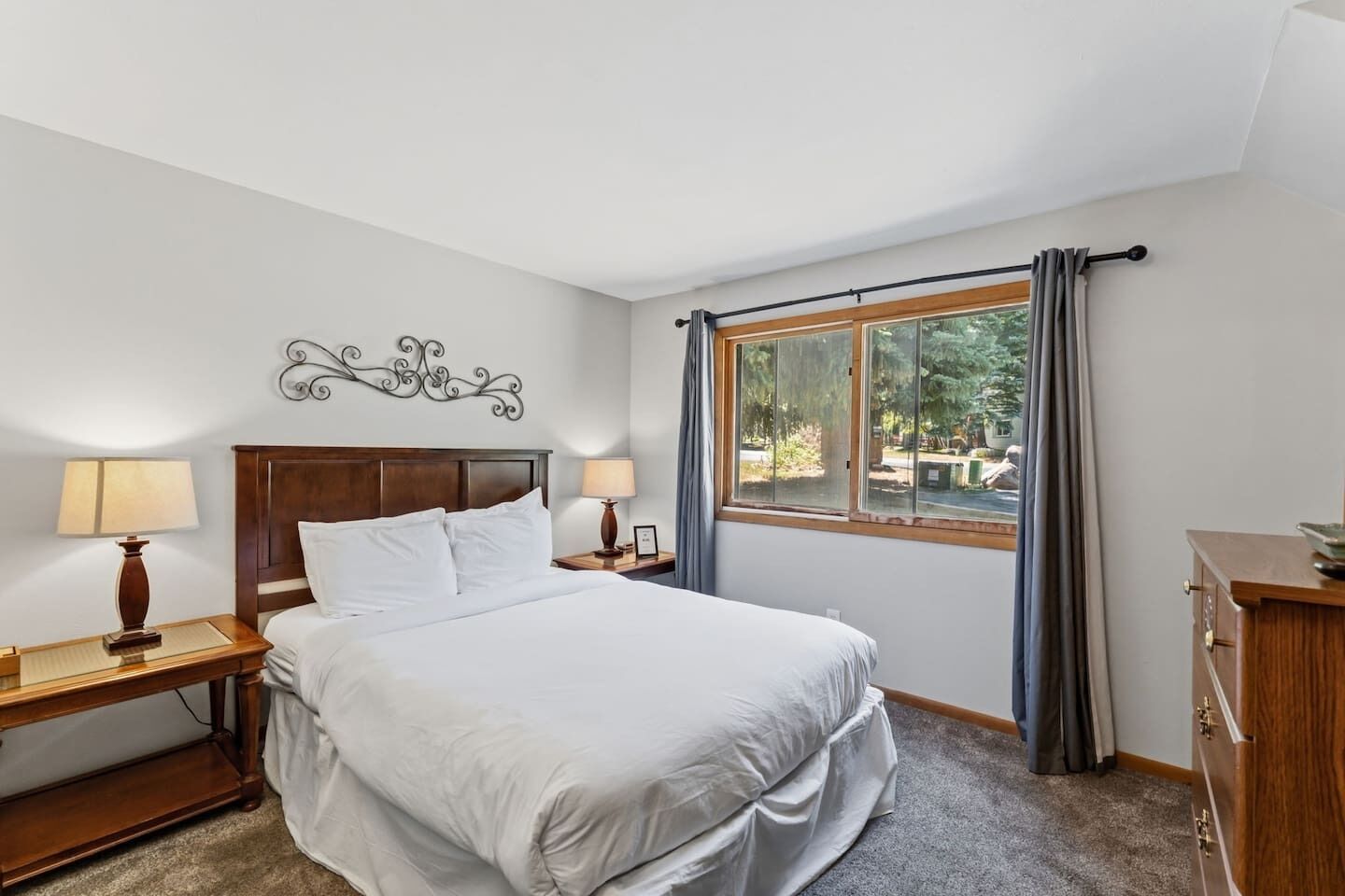 Habitación de hotel con una cama grande, dos mesitas de noche con lámparas, una ventana con cortinas y un adorno en la pared.