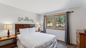 Habitación de hotel con una cama grande, dos mesitas de noche con lámparas, una ventana con cortinas y un adorno en la pared.