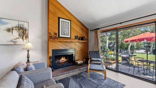 Ein Wohnzimmer mit Kamin, einer Couch, einem Sessel und einer großen Glasschiebetür zu einer Terrasse mit Grill.