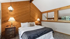 Ein Schlafzimmer mit Holzbalkendecke, einem Bett mit weißer Bettwäsche, zwei Nachttischlampen, einem Nachttisch mit Lampe und einem Fenster mit Blick.