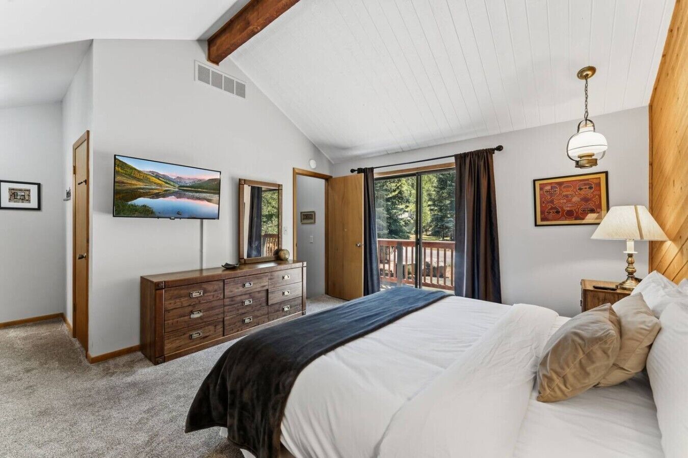 Un dormitorio con una cama grande, un aparador, un televisor y un balcón con vistas.