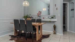 Un espace repas comprenant une table en bois, des chaises noires, un tapis en peau de vache et des luminaires suspendus.