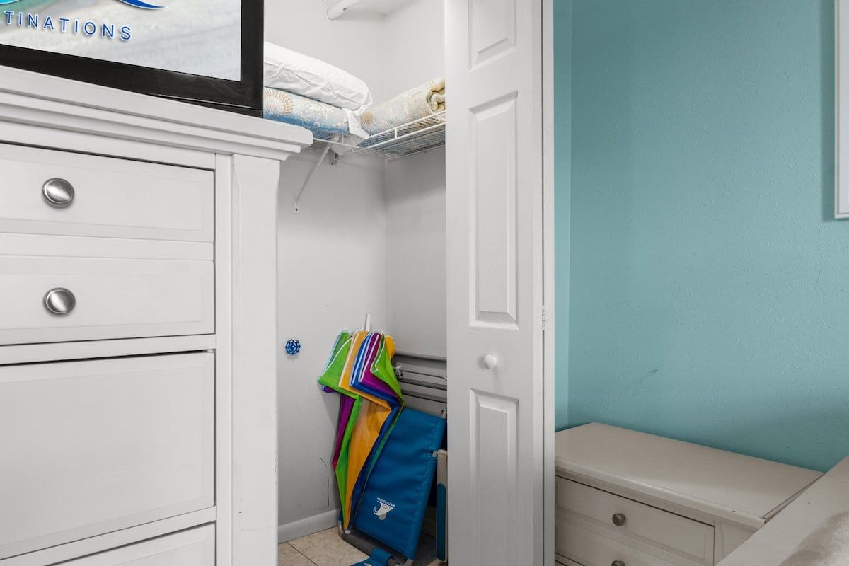 A room with a white wardrobe, a bed with a blue wall, and a door leading to another room.