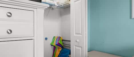 Una habitación con un armario blanco, una cama frente a una pared azul, y una puerta que da a otra estancia.