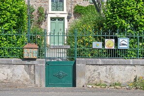 A green gate with a sign reading 'BALADOUX' and a small building with a red roof behind it.