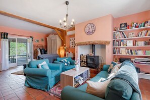 A cozy living room with teal sofas, a wooden coffee table, a fireplace, and a bookshelf filled with books.