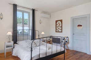 A bedroom with a metal bed frame, two bedside tables with lamps, a chair, a door, and a window with curtains.