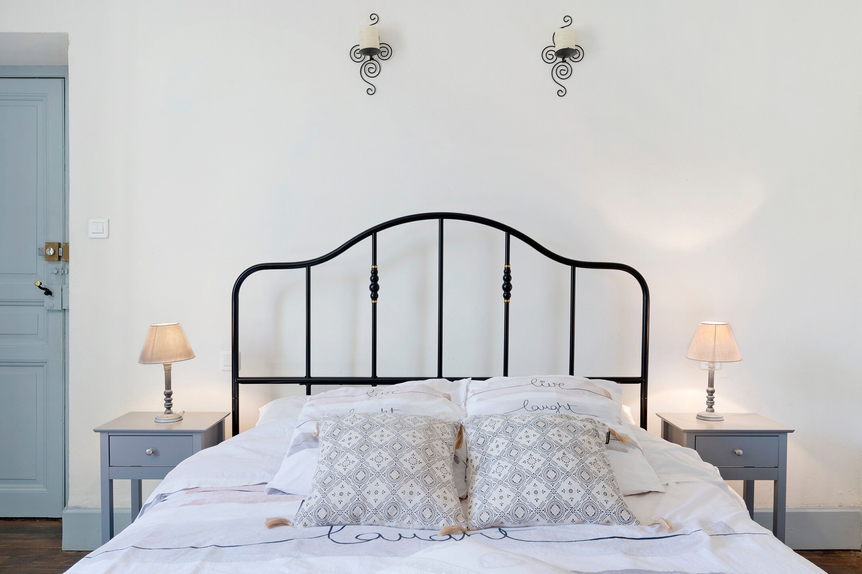 A bed with a black metal frame, two bedside tables with lamps, patterned pillows, and a light blue door.