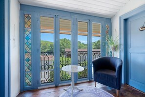 A room with a blue door, a chair, a small table, and a view of a green landscape.